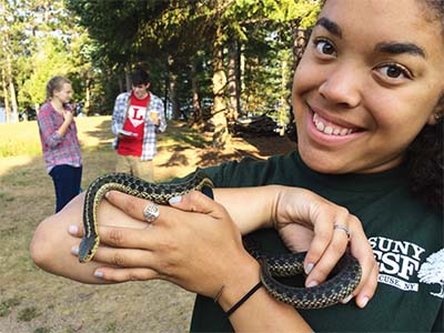 Jet Lewis holding a snake. There are two students in the background