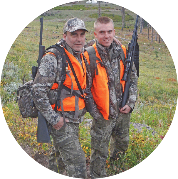 Two men in camoflauge and orange vests with guns over their shoulders