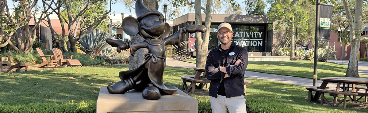 Ben with arms crossed standing next to bronze statue of mickey mouse 