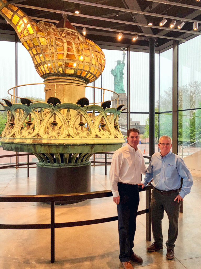 Jeffrey Rainforth ’97 and partner Dougas Phelps stand in front of the orginal torch of the Statue of Liberty, Inspiration Gallery, Statute of Libetry Museum.