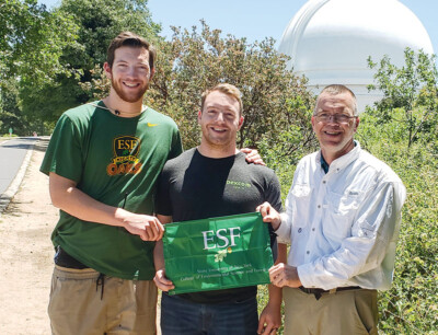 Doug Daley (ERE) displays the ESF flag at the Palomar Observatory in California with sons Cameron (’22, ERE) and Bryan (SU, 2015).