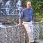 John Bartow leaning on a bridge. There is a waterfall behind him