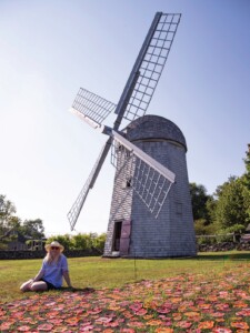 Eileen Travis sitting beside “The Poppy Field” installation with the Jamestown Windmill in the background. Inspired by Flanders Field in Belgium